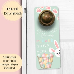 May include: A light blue door hanger with a white bunny peeking out from the right side. The bunny has pink ears and a pink nose. The hanger has the text "Dear Easter Bunny PLEASE STOP HERE!" in colorful letters. There are also pastel colored eggs in a basket and paw prints in the background.