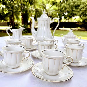 May include: A complete white porcelain tea set with gold trim, including a teapot, creamer, sugar bowl, and multiple teacups and saucers. The set is arranged on a white tablecloth, perfect for a tea party.