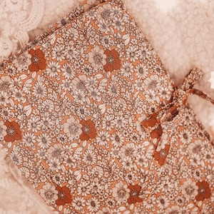 May include: Folded floral fabric featuring a pattern of white and rust-coloured flowers on a peach background. A matching fabric tie is visible on the right. The fabric is likely for sewing or crafting projects.