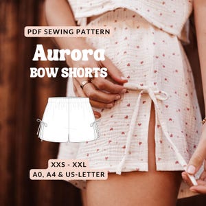 May include: A PDF sewing pattern for "Aurora Bow Shorts" is displayed. The image shows a sketch of the shorts with bow details, and the text "XXS - XXL" and "A0, A4 & US-LETTER". The shorts are part of a sewing pattern.