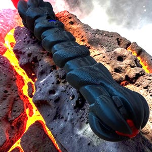 May include: A black, textured, dragon-claw-shaped object with a blue gem and red accents. The object is set against a backdrop of volcanic rock and lava, creating a fantasy or sci-fi theme.