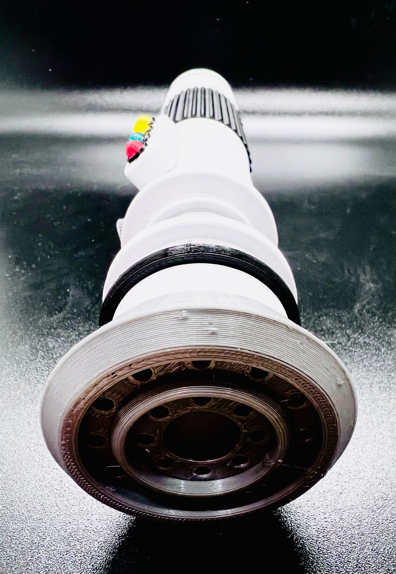 Puede incluir: Un sable de luz blanco con un mango negro y una punta plateada. El sable de luz tiene una serie de anillos negros alrededor del mango y una serie de peque&ntilde;os agujeros alrededor de la punta.