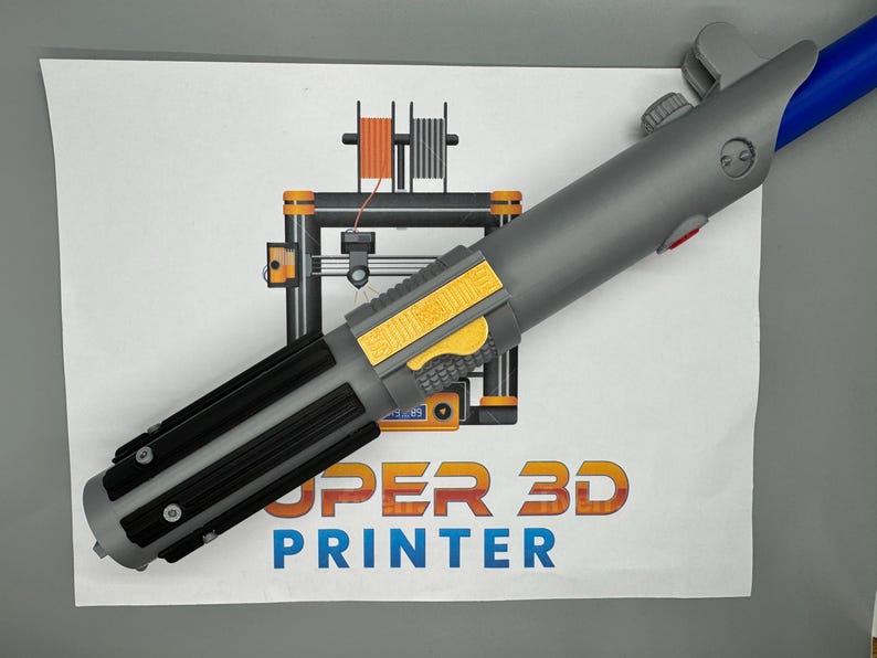 May include: A gray and black lightsaber prop with a yellow and black detail on the handle. The lightsaber is on a white surface with a 3D printer illustration and the text "SUPER 3D PRINTER".