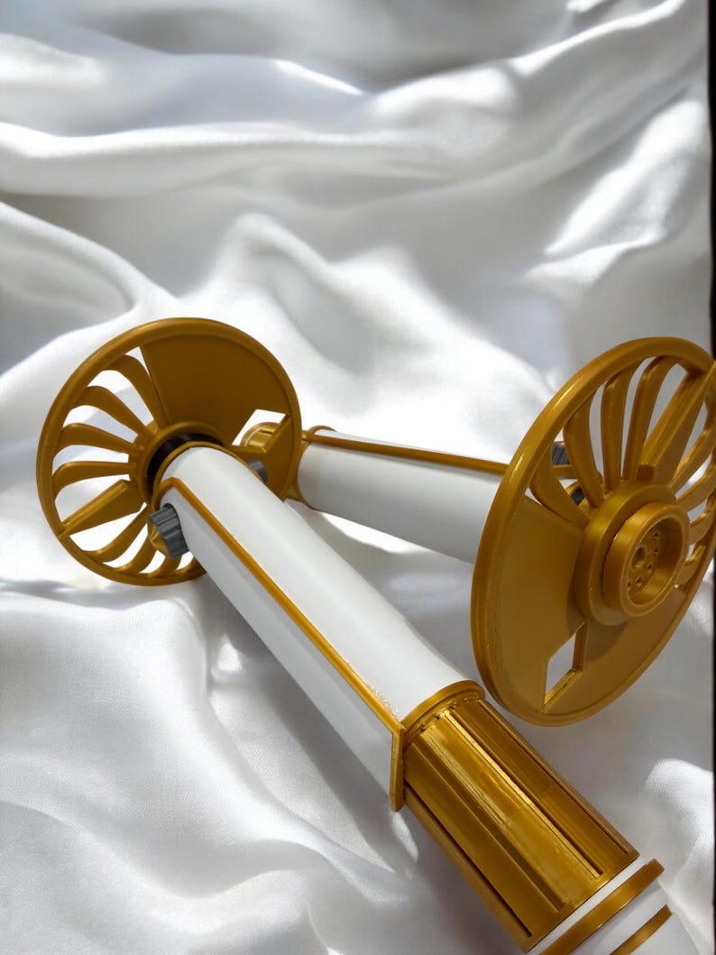 K&ouml;nnte beinhalten: Zwei dekorative, gold-wei&szlig; Objekte mit einem f&auml;cherartigen Design. Die zylindrischen wei&szlig;en K&ouml;rper sind mit Gold akzentuiert. Der Hintergrund ist ein wei&szlig;er, seidiger Stoff.