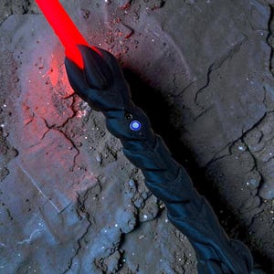 May include: A black lightsaber with a textured handle and a glowing red blade. The hilt features a blue button and a claw-like design at the blade's base. The lightsaber is set against a dark, textured background.
