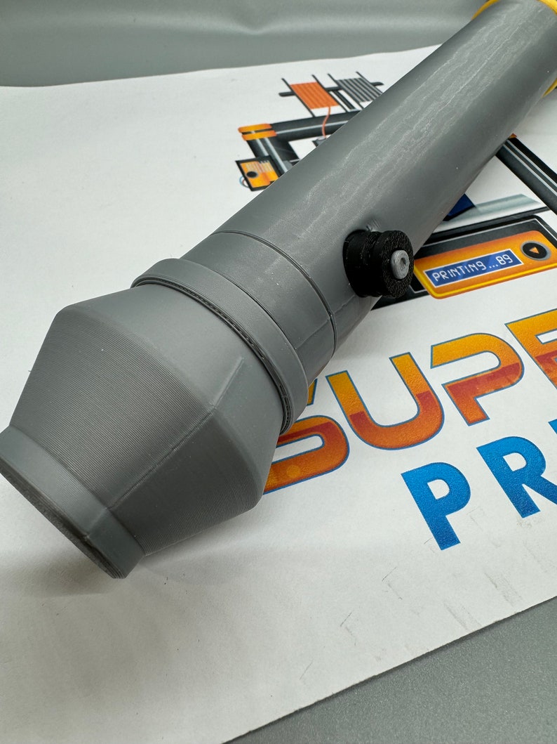 May include: A grey 3D printed nozzle with a black knob on the side. The nozzle is designed for a 3D printer and has a round opening at the end.