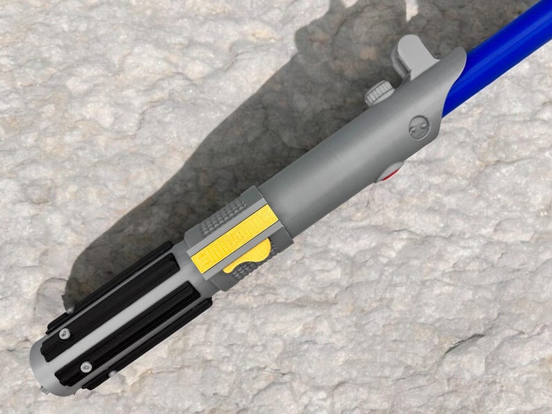May include: A gray lightsaber toy with a black handle and a yellow button. The lightsaber has a blue blade that is not visible in the image.