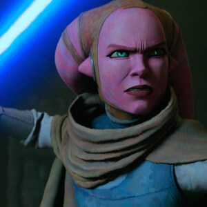 May include: A pink-skinned character with green eyes holds a glowing blue lightsaber. She wears a blue and tan outfit with a tan scarf. Her expression is one of intense focus, with a furrowed brow and a determined gaze.