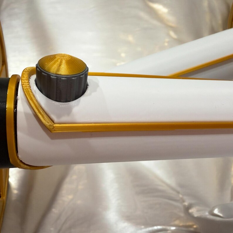 K&ouml;nnte beinhalten: Nahaufnahme eines wei&szlig;-goldenen Objekts mit zylindrischer Form. Das Objekt hat einen goldfarbenen Rand und eine goldfarbene, geriffelte Oberseite. Auf dem Objekt ist eine dunkelgraue Kappe zu sehen. Das Objekt ist vor einem wei&szlig;en Hintergrund platziert.