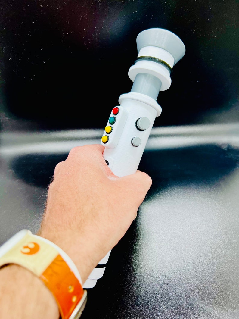 Puede incluir: Un accesorio de sable de luz blanco con un mango negro y gris, un bot&oacute;n negro y blanco y una perilla negra y blanca. El sable de luz tiene cuatro luces de colores: rojo, amarillo, verde y azul.