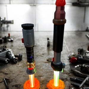 May include: Two lightsaber props with orange glowing blades, one with a red tip and the other with a green tip, standing on orange bases.