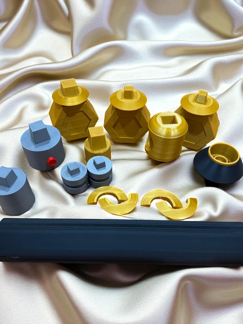 May include: An assortment of 3D-printed objects in various shapes and colors. The collection includes gold-colored hexagonal containers with square lids, gray cylinders, and a long, rectangular dark blue object. Also, there are gold-colored curved shapes.