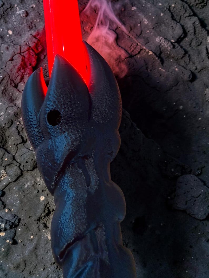 May include: A black, stylized lightsaber hilt with a red blade emitting a bright glow. The hilt has a textured, claw-like design. Smoke-like vapor rises from the blade, creating a dramatic effect. The background is dark and textured.