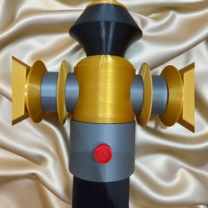 May include: A 3D-printed object with a complex design. The object features a combination of colors, including gold, gray, black, and red. It has a cylindrical body with circular elements and a button. The object is likely a decorative or functional item.