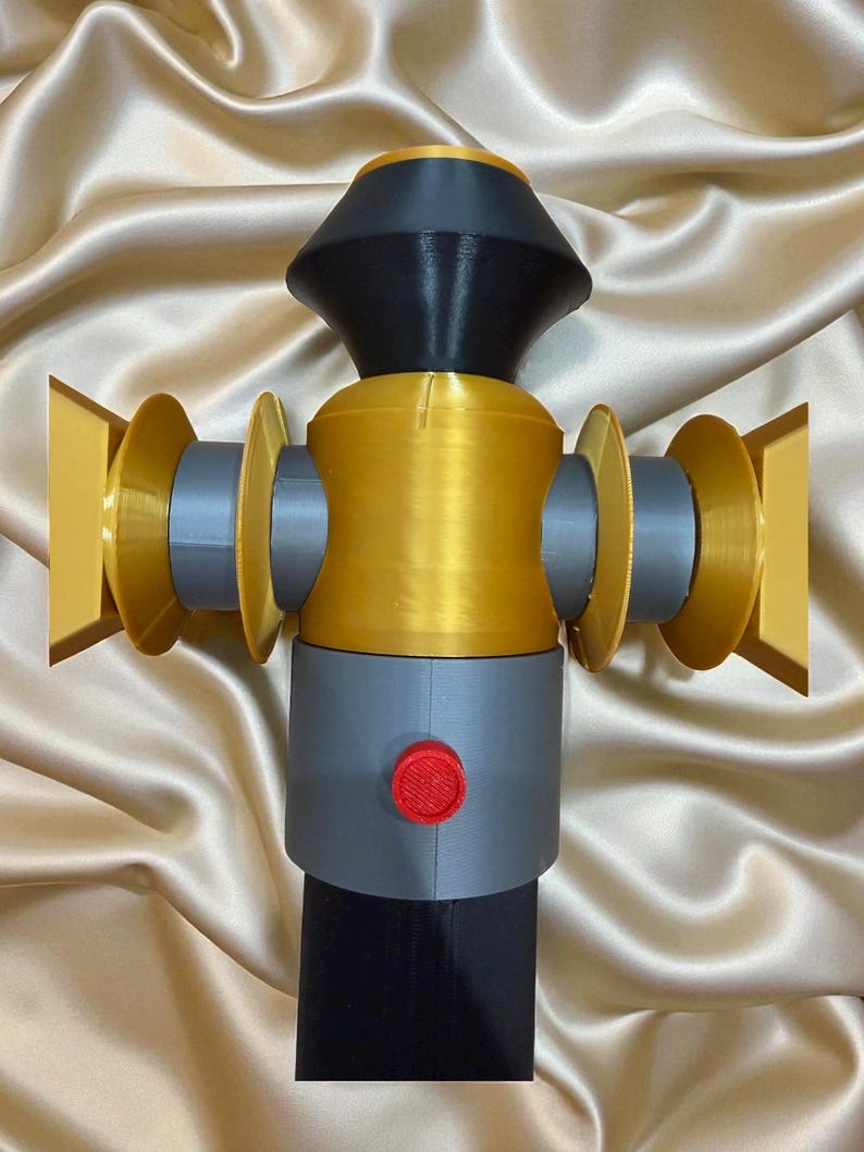 May include: A 3D-printed object with a complex design. The object features a combination of colors, including gold, gray, black, and red. It has a cylindrical body with circular elements and a button. The object is likely a decorative or functional item.