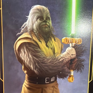 May include: Illustration of a Wookiee character holding a green lightsaber. The Wookiee is depicted with gray fur, wearing a yellow tunic and brown pants. The lightsaber has a gold handle.