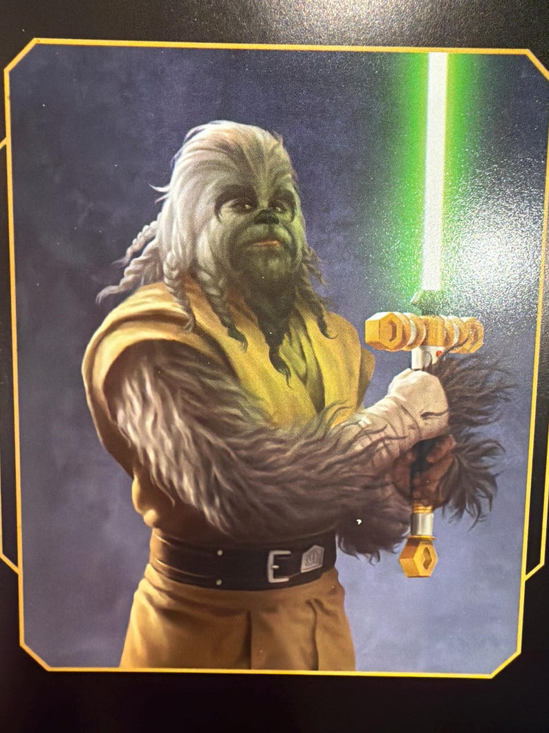 May include: Illustration of a Wookiee character holding a green lightsaber. The Wookiee is depicted with gray fur, wearing a yellow tunic and brown pants. The lightsaber has a gold handle.