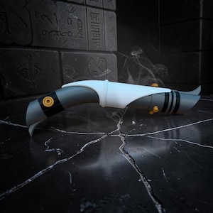 K&ouml;nnte beinhalten: Ein futuristisches, stilisiertes Lichtschwert-Requisit in Grau-, Wei&szlig;- und Gelbt&ouml;nen. Der Griff hat ein schlankes Design mit einem gebogenen Klingenschutz und kreisf&ouml;rmigen gelben Akzenten. Das Requisit steht vor einem dunklen, strukturierten Hintergrund.