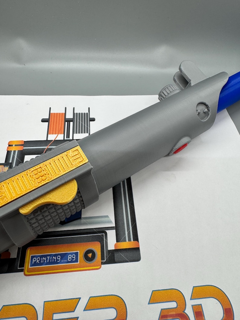 May include: A 3D printed gray lightsaber with a yellow and orange handle. The lightsaber is being printed on a 3D printer with the text "PRINTING...89" displayed on the screen.