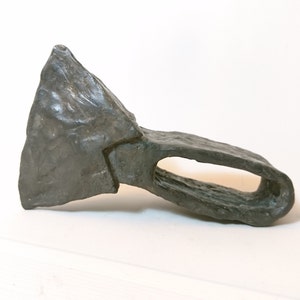 May include: A gray metal axe head with a triangular blade and a handle with a hole for a shaft.