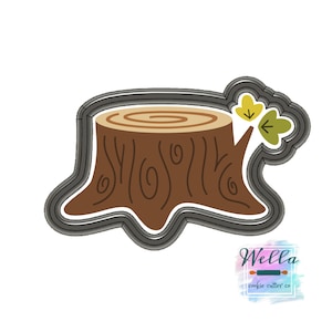 May include: A brown tree stump cookie cutter with a gray outline and two yellow leaves on the side. Wella cookie cutter co.