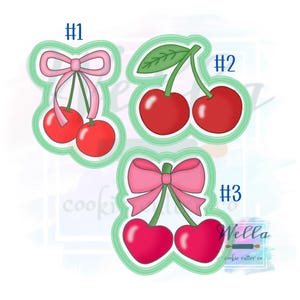 Puede incluir: Tres diseños de cortadores de galletas con temática de cerezas. Cada diseño presenta dos cerezas rojas con tallos y hojas verdes o lazos rosas. Los diseños están delineados en verde y numerados.