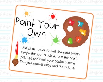 以下が含まれることがあります： 「Paint Your Own」のテキストと指示が書かれた長方形のサイン。茶色の画家のパレットとカラフルなペイントの飛沫、筆が描かれています。サインはオレンジ色で縁取られています。