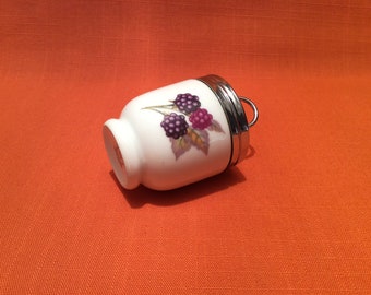 Könnte beinhalten: Ein weißer Eierbecher aus Keramik mit einem silbernen Deckel und einem Brombeer-Design. Der Eierbecher steht auf einer leuchtend orangenen Oberfläche.