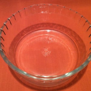 Peut inclure: Un plat à four en verre transparent avec un bord cannelé. Le plat est vide et posé sur une surface rouge.