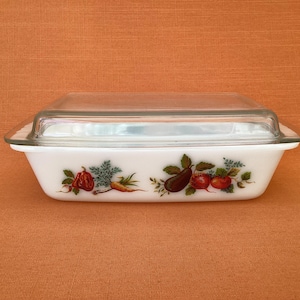 Op de afbeelding: Een rechthoekige witte glazen ovenschaal met een doorzichtig glazen deksel. De buitenkant van de witte schaal is voorzien van een kleurrijke botanische print van diverse groenten, waaronder rode paprika's, wortels, aubergines en tomaten.