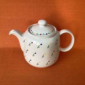 May include: White ceramic teapot with a lid, decorated with a scattered pattern of small green stems and red, yellow, and blue flowers.