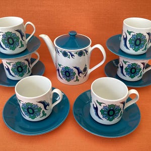 以下が含まれることがあります： ティール色の蓋が付いたティーポットと、6客のカップ＆ソーサーからなる陶磁器のティーセット。各アイテムは白いベースに、ティール、ダークブルー、グリーンの色合いで繰り返される花柄が施されています。ソーサーは無地のティール色です。