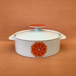 Könnte beinhalten: Weiße Keramik-Auflaufform mit Deckel und einem floralen Design in Orange und Rot. Die Form hat zwei Griffe.