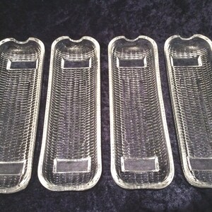 May include: Four clear glass serving dishes with a woven texture. Each dish is rectangular with a curved top and a rectangular indentation in the centre. The dishes are arranged side by side.