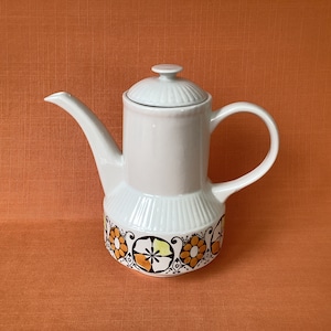 Könnte beinhalten: Weiße Kaffeekanne aus Keramik mit einem floralen Design in Orange, Gelb und Braun. Die Kanne hat einen Deckel und einen Griff.