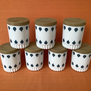 May include: Set of six white ceramic canisters with brown wooden lids and a blue and gold pattern. The canisters are arranged in two rows of three.