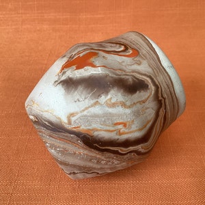 May include: A white ceramic vase with brown and orange marbling. The vase has a unique, geometric shape.