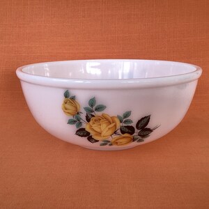 May include: White mixing bowl with a yellow rose floral design. The bowl is made of glass and has a rounded shape.