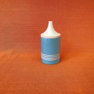 May include: A blue and white ceramic container with a conical lid. The cylindrical body of the container is light blue with three white horizontal stripes. The lid is white. The container is set against an orange background.