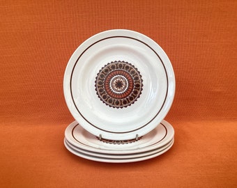 May include: A set of three white ceramic plates with a brown and orange geometric design. The plates are stacked on top of each other.