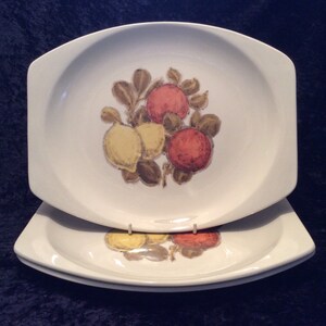 May include: Three white ceramic dinner plates with a raised rim and a design of yellow lemons and red oranges on a branch with green leaves.