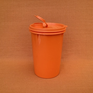 May include: An orange plastic container with a flip top lid. The container is cylindrical and has a smooth surface.