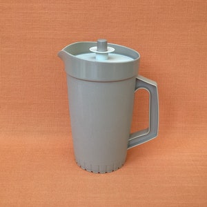 Könnte beinhalten: Eine graue Plastikkanne mit Deckel und Henkel. Die Kanne hat eine strukturierte Oberfläche und einen gerippten Boden.