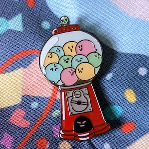 May include: A red gumball machine with a skull on top. The gumball machine is filled with colorful gumballs with different facial expressions.