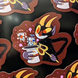May include: A red and black cartoon devil character holding a golden trident. The devil is wearing a top hat and has a mischievous grin. The background is a dark red with pink stars and a white cup with a halo.