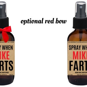 May include: Two brown glass spray bottles with a brown paper label that says "SPRAY WHEN MIKE FARTS" in black and red text. The label also says "ROOM AND LINEN SPRAY" in smaller black text. The bottles have black spray tops and are tied with a red bow.