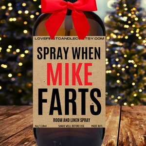 May include: A brown glass bottle with a red bow and a label that reads "SPRAY WHEN MIKE FARTS" in black and red text. The label also says "ROOM AND LINEN SPRAY" and "4oz/118ml".