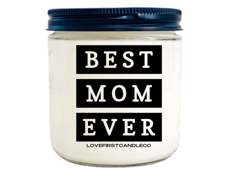 May include: A white candle jar with a black lid. The jar has a black label with the text "BEST MOM EVER" in white letters. The label also includes the text "LOVEFIRSTCANDLECO" in smaller white letters.