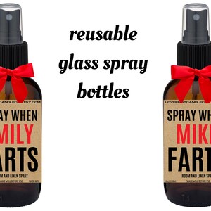 May include: Two brown glass spray bottles with red bows. The labels are brown with white text that reads "SPRAY WHEN [NAME] FARTS" and "ROOM AND LINEN SPRAY". The text "reusable glass spray bottles" is written in black above the bottles.