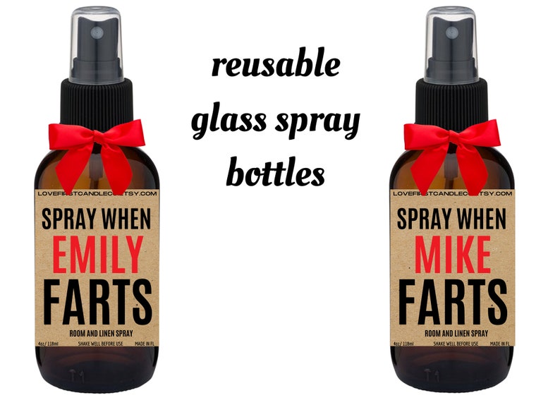 May include: Two brown glass spray bottles with red bows. The labels are brown with white text that reads "SPRAY WHEN [NAME] FARTS" and "ROOM AND LINEN SPRAY". The text "reusable glass spray bottles" is written in black above the bottles.